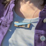 Person wearing a blue retro mcm house-shaped necklace with a purple jacket