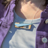 Person wearing a blue retro mcm house-shaped necklace with a purple jacket