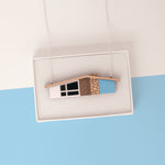 Blue midcentury house necklace on silver chain draped over a white gift box on a light blue and white background