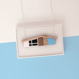 Blue midcentury house necklace on silver chain draped over a white gift box on a light blue and white background