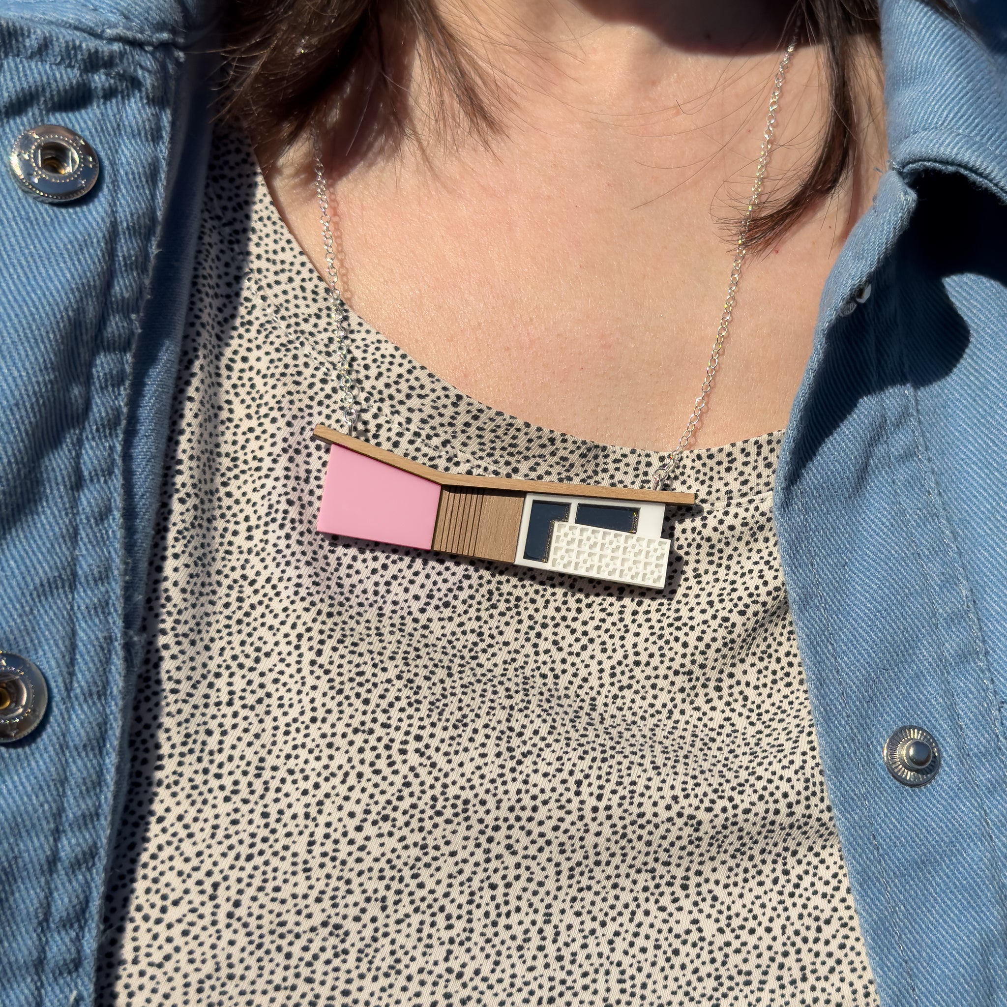 Person wearing a pink house-shaped necklace on a patterned shirt and denim jacket.