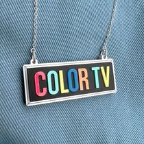 A vintage-style COLOR TV sign necklace with rainbow-colored letters, attached to a silver chain.