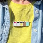 Necklace with white palm springs house design worn by a person in a yellow tshirt and denim shirt.