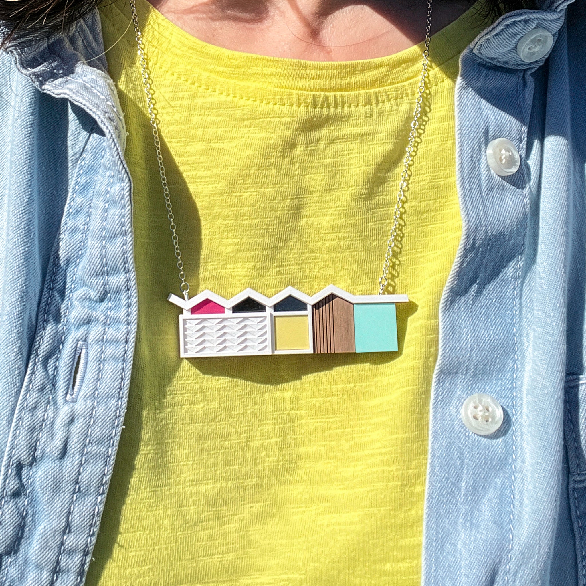 Necklace with white palm springs house design worn by a person in a yellow tshirt and denim shirt.