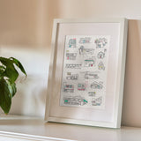A framed art print featuring hand-drawn line art illustrations of retro roadside buildings and storefronts. Styled on a white shelf next to a green plant against a neutral beige wall.