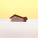 A miniature midcentury-era coffee shop brooch made from wood and acrylic, set against a plain white and yellow background.