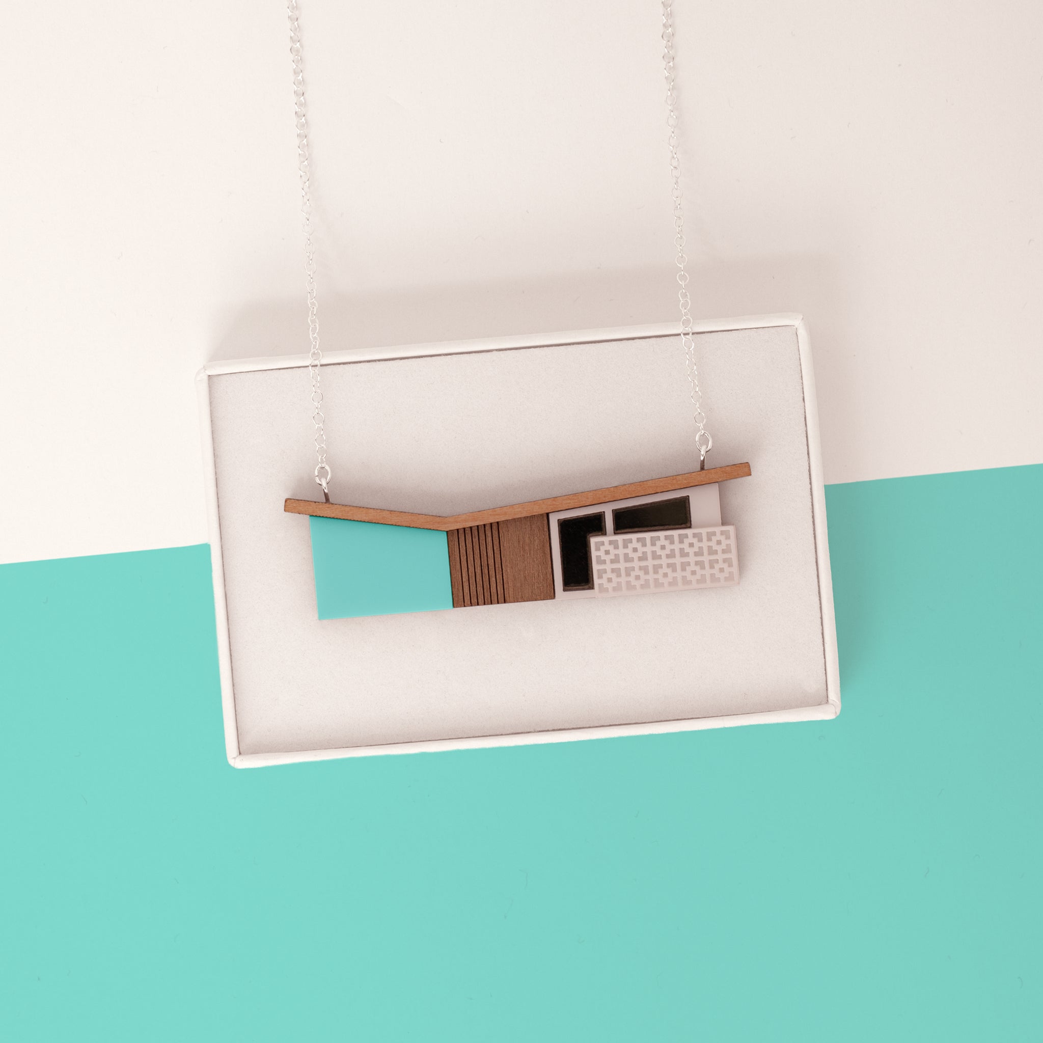 Midcentury house necklace with tiny breeze blocks draped over a white gift box on a mint background