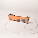 Close up of a retro house-shaped necklace with orange acrylic roof and silver chain set on a white background
