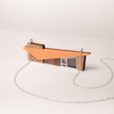 Close up of a retro house-shaped necklace with orange acrylic roof and silver chain set on a white background
