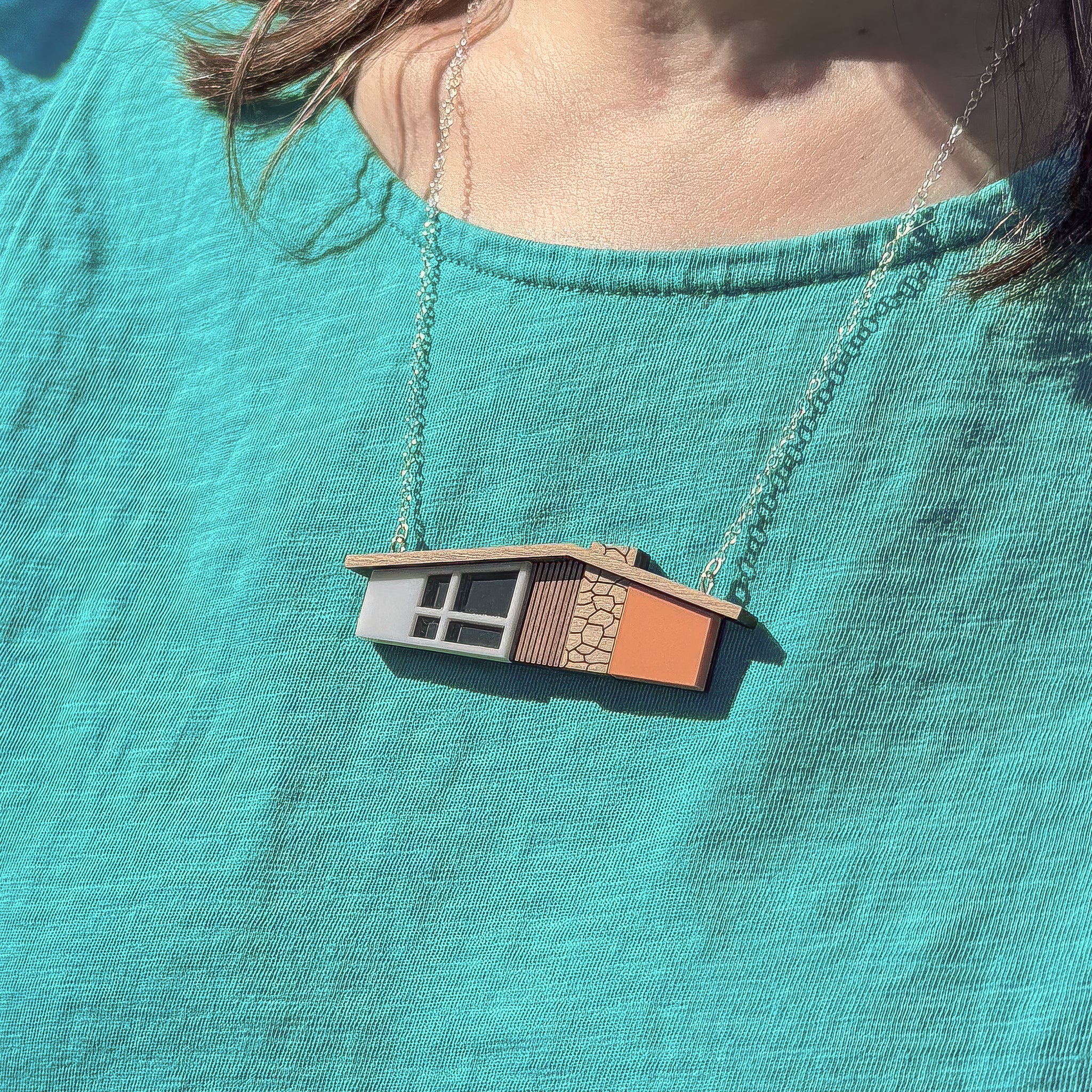 Necklace with an orange midcentury house-shaped pendant on a person wearing a teal t-shirt