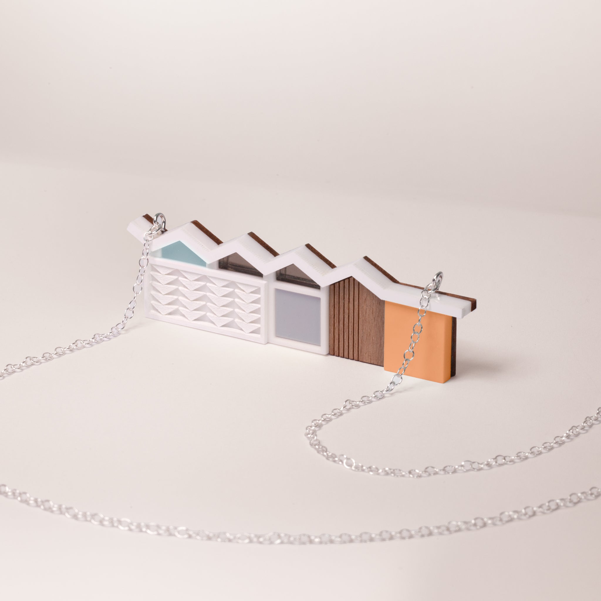 Small model of a modernist house mader from acrylic and wood with silver chain on a beige background