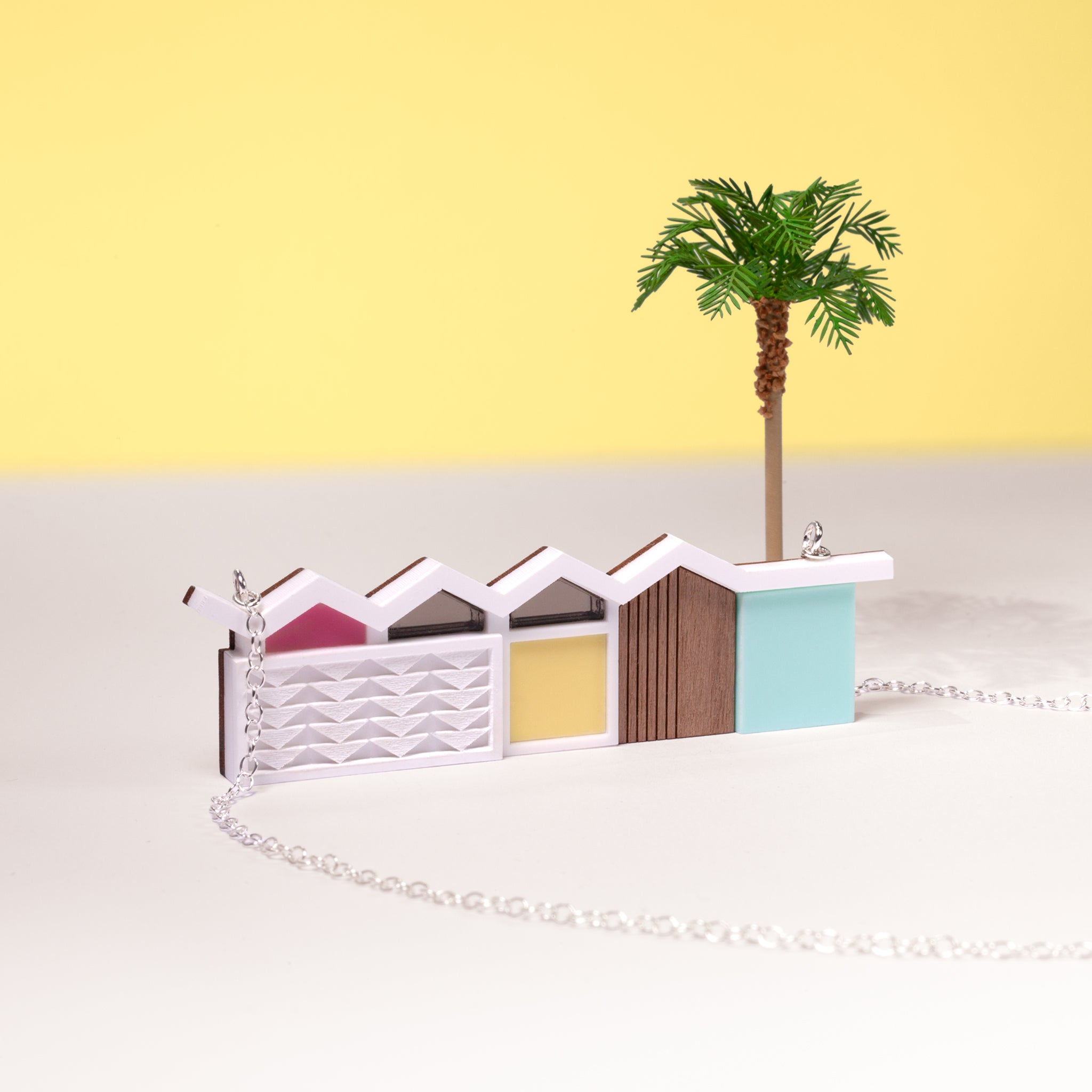 Close up of a palm springs house necklace with silver chain and palm tree on a yellow background