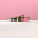 Pink wooden midcentury house necklace with silver chain on a plain pink background