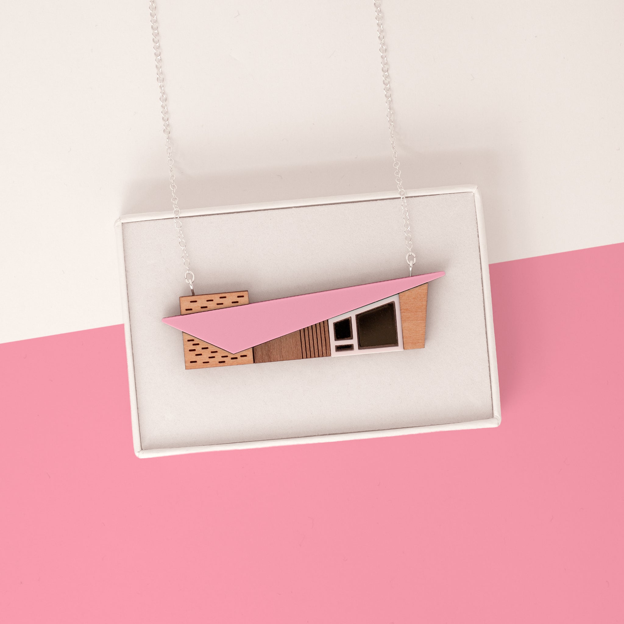 Pink miniature house pendant with a midcentury modern shape in a white gift box on a pink background