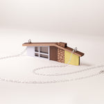 Miniature yellow ranch house pendant with silver chain on a white background