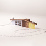 Miniature yellow ranch house pendant with silver chain on a white background
