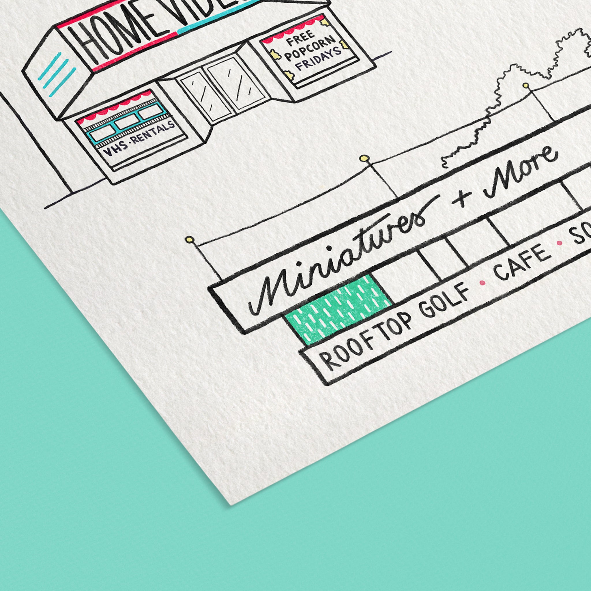 A close-up of a white textured paper art print featuring a hand-drawn black ink illustrations of midcentury roadside buildings such as a 'HOME VIDEO' store, mini golf and cafe. Set against an aqua background.