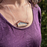 Woman wearing the wooden miniature roadside coffee shop necklace on a sterling silver chain