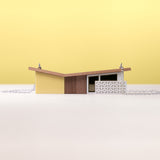 A miniature model of a yellow modernist house on silver chain against a yellow background
