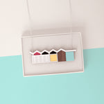 Colourful house pendant with zigzag roof draped over a white gift box on a light blue and white minimalist background